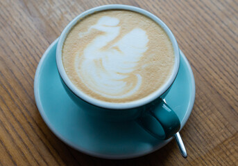 A cup of cappuccino on a wooden table. Close-up of a blue cup of coffee with milk foam.