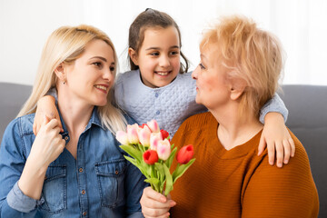 Photo portrait of granddaughter congratulating granny giving tulips bunch sitting near mom