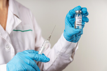 Vial withCOVID-19 vaccine and a syringe with a needle for injections for coronavirus infection in the hand of a doctor in a nitrile glove on a white background. Close-up. Concept fighting Coronavirus