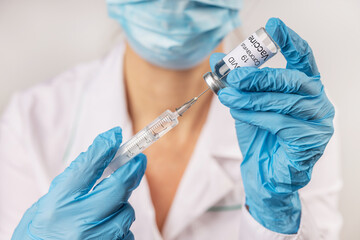 Vial withCOVID-19 vaccine and a syringe with a needle for injections for coronavirus infection in the hand of a doctor in a nitrile glove on a white background. Close-up. Concept fighting Coronavirus