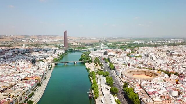 Drone flying above the famous Guadalquivir River in the center of Seville City, At right the Bull Ring and Theatre of Seville. In front Triana Bridge. Drone forward, beautiful perspective of the city.