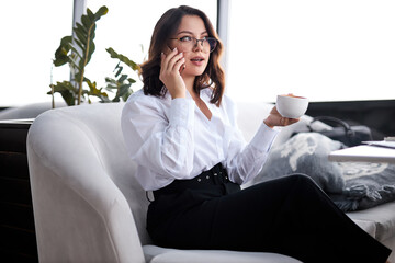 Young attractive woman with cute smile talking on mobile phone while sitting alone in coffee shop during break time