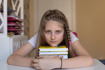 A pretty blonde girl put her head on a stack of colorful books, she is in her room, loves to read....