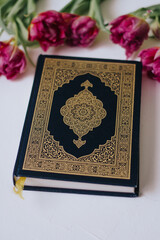Fototapeta premium Holy Quran on a white background with flowers. Tulips. Ramadan. Hatm of the Qur'an. Reading the Quran. Ramadan concept. Islamic concept