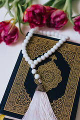 Holy Quran and rosary on a white background with flowers. Tulips. Ramadan. Hatm of the Qur'an. Reading the Quran. Ramadan concept