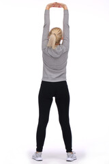 The young girl exercises by stretching and raising both her arms up. Rear view