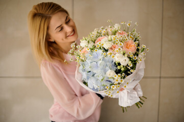 blonde woman holds bouquet of roses and hydrangeas and small daisies and looks at it