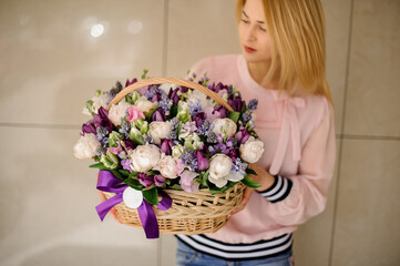 large wicker basket with peonies and tulips decorated with ribbon in hands of blonde woman