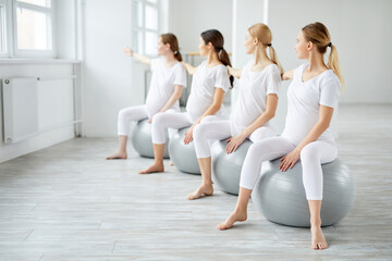 Fototapeta premium Side view on beautiful caucasian women in sportive outfit exercising on fitball