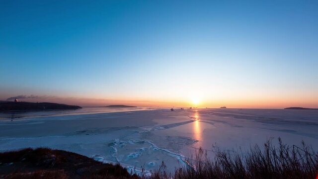 Timelapse of frozen Eastern Bosphorus strait and ships on the background. The bright winter sun is rising above the sea. Vladivostok, Russia