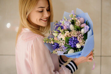 happy blonde woman holds floral bouquet of different fresh spring flowers in her hands