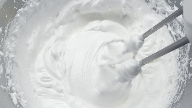 Beaten egg white. Whipped cream white in bowl and mixer, top view.