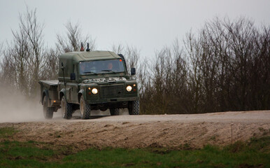 british army land rover defender 4x4 with attached trailer speeds along a dusty stone track
