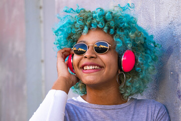 portrait of hispanic afro american woman with headphones and mobile phone smiling on the street