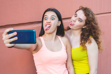 two young woman taking pictures with their mobile phone and making grimaces, two sisters make...