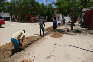 Non-identifiable workers laying fiber optic cables by hand in the soil of the village of...