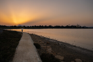 A woman walks at sunset along a footpath on Larnaca salt lake shore with the Hala Sultan Tekke mosque in the background