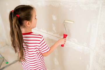 Side view of child girl priming and painting walls with roller during house renovation. Home repairs with family. Update, improvement living room with kids. Selective focus on roller