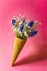 Ice cream cone with flowers on pink background. Side view, copy space, spring flowers concept