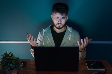 Young man in front of a computer doing work from home. All in a low light environment