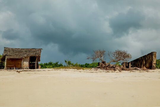 several old ruined African huts with roofs of palm branches stand on the ocean under the searing sun