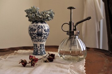 Close-up of a fancy perfume bottle and small flower vase with green leaves on a wooden antique...