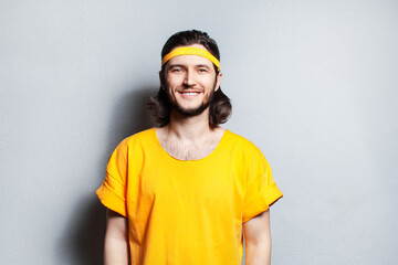 Portrait of young smiling guy in yellow shirt on background of grey wall.