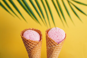 Two strawberry ice creams in a cone on a yellow background. Tropical leaf