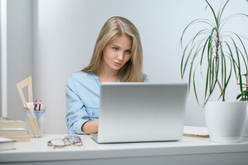 Fototapeta premium A girl with a laptop is studying at an online school. White room background