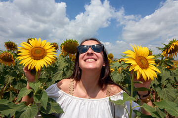 A cheerful beautiful Turkish woman in sunglasses posing on a sunflower field