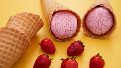 Strawberry ice cream in a waffle cone. Ice cream and berries on a yellow