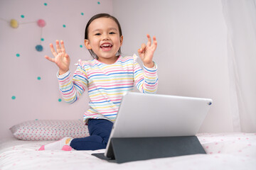 Happy young child playing  on the bed using her tablet