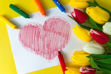 Big red heart drawn on paper, crayons pencils and bouquet of flowers colorful tulips on yellow background. Child prepare surprise for Mom on Happy Birthday, Women`s Day, Mother's Day.