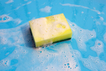Dishwashing sponge with foam on blue background.