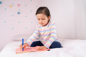 Beautiful little girl drawing in her room.