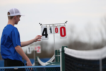 A high school tennis player changes the score between games.