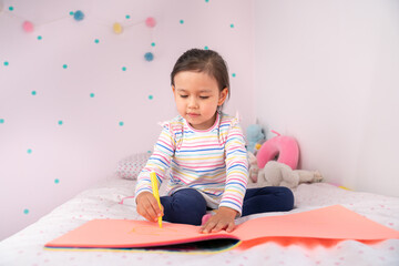 Toddler girl drawing on the bed in her room, writing and painting