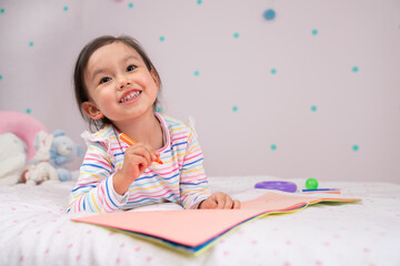 Cute young child smiling while thinking and drawing.  
