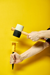 Rubber mallet and chisel in male hands isolated on yellow background