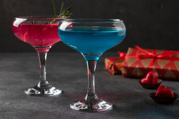Two glasses of shimmering pink and blue champagne and heart-shaped candies on a dark background. Romantic dinner for a couple.