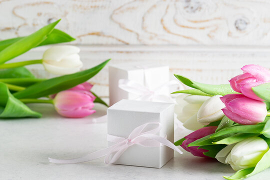 Beautiful spring composition with fresh tulips and gift boxes on light wooden background close up. Mother’s Day greeting card.