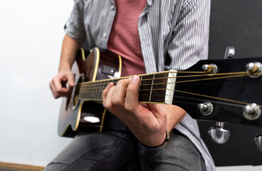 Male musician is playing music on wooden acoustic guitar, capture chords by finger.