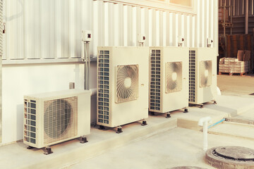 Condenser unit or compressor outside industrial plant building. Unit of central air conditioner (AC) or heating ventilation air conditioning system (HVAC). Electric fan and refrigerant pump inside.