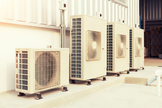 Condenser unit or compressor outside industrial plant building. Unit of central air conditioner (AC) or heating ventilation air conditioning system (HVAC). Electric fan and refrigerant pump inside.