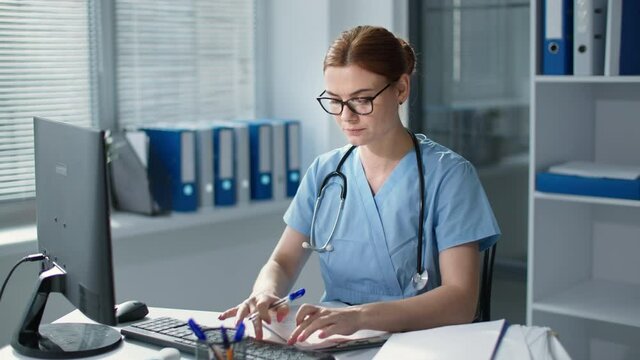 unhappy female therapist in glasses works at the computer in the hospital, sad girl in medical uniform feels a pain in the neck sitting at the table