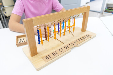 Girl in striped is playing and sorting a puzzle of colored plastic beads in montessori school.
