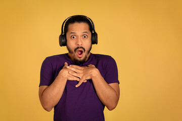 Obraz premium Portrait of man with funny face using headphone with yellow background. Man with surprised face.