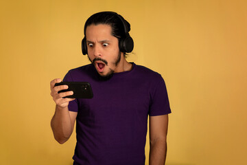 Portrait of man using headphone with yellow background. Man with surprised face using smartphone