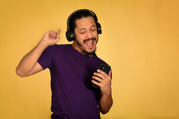 Portrait of man singing and using headphones with yellow background