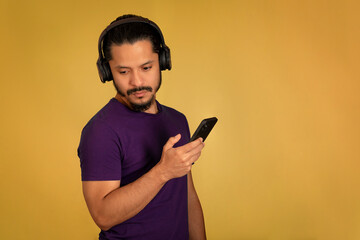 Portrait of man using headphone with yellow background. Man using smartphone